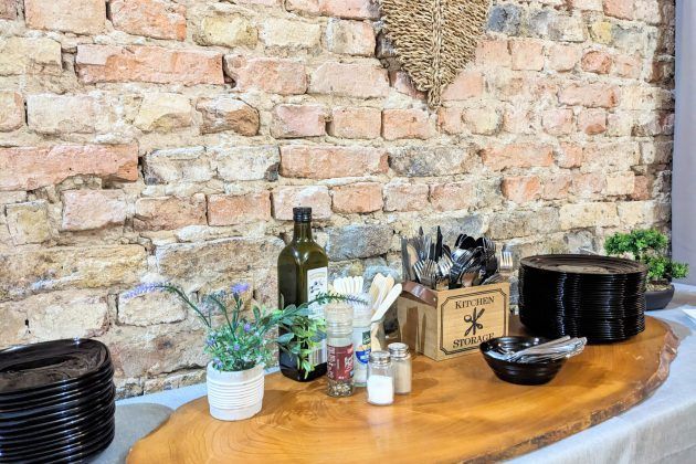 Gedeckter Cateringtisch mit Geschirr und Besteck vor Backsteinwand